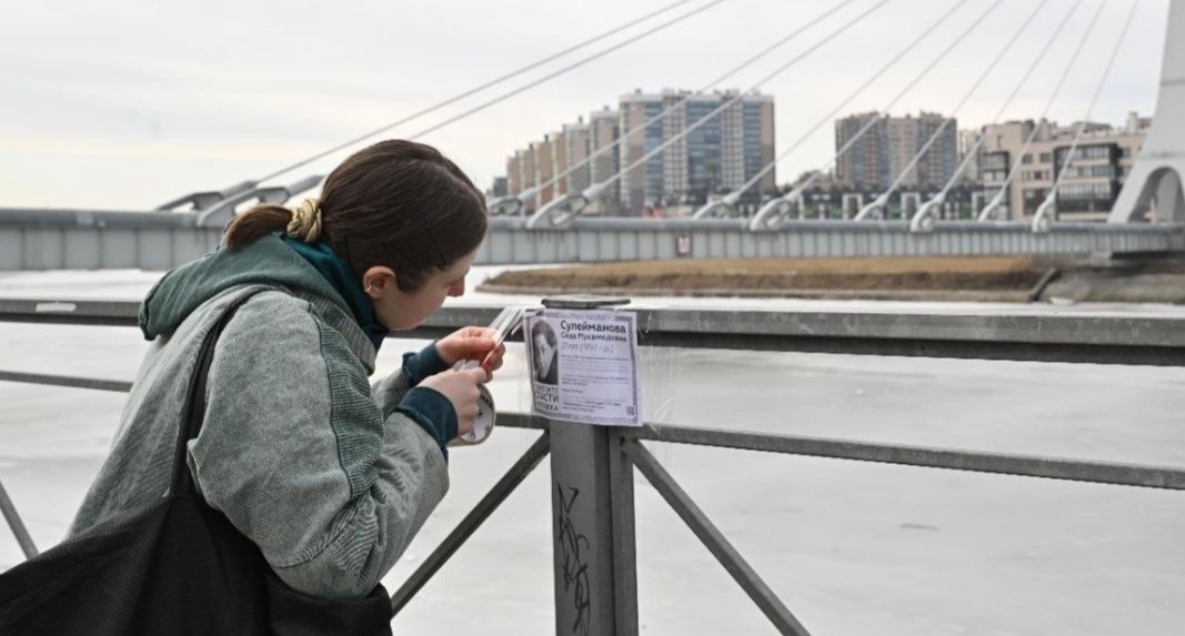 Елена Патяева наклеивает  листовку на перила моста. Санкт-Петербург, 8 марта 2025 года. Фото из телеграм-канала Елены Патяевой https://t.me/helpseda/313